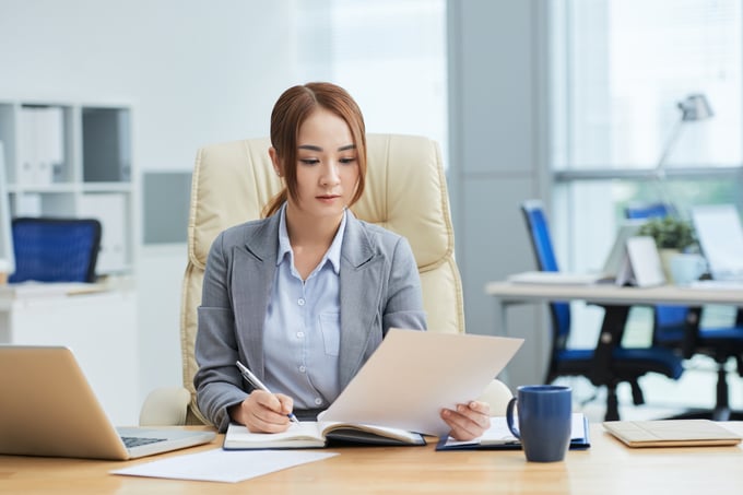 medium-shot-young-asian-woman-suit-sitting-desk-office-reading-document
